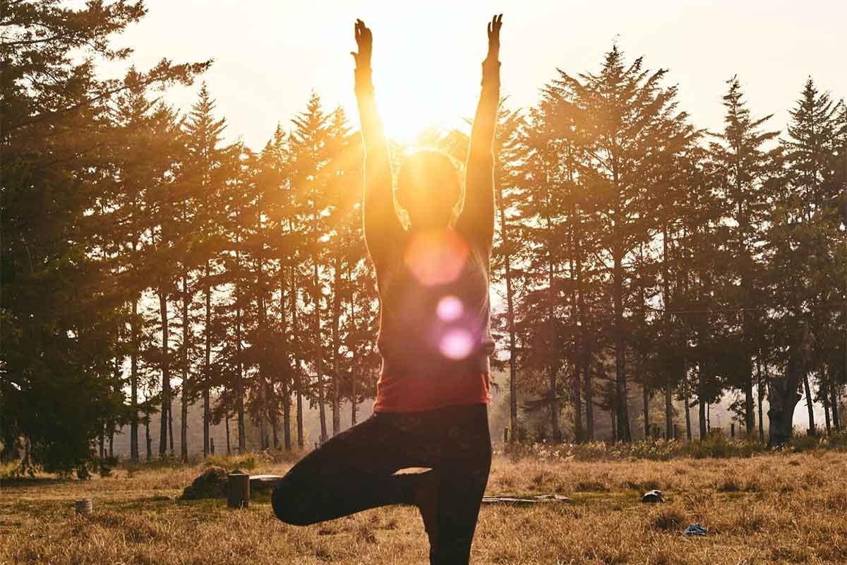 A person in a yoga pose with the sun setting behind them.