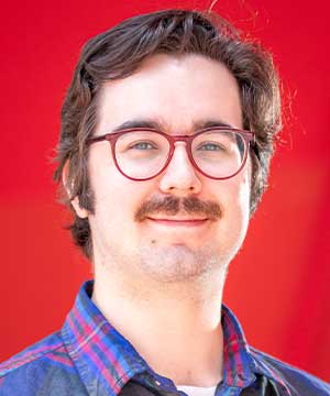 A headshot of Paul Hedreen, a man with glasses and a mustache on a red background.