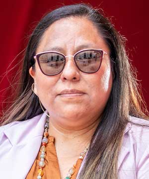 Headshot of Fabiola Mendieta-Cuapio, an indigenous woman, brown skin, with long dark hair, and red glasses. Mendieta-Cuapio looks directly at the camera in the warm sunlight.