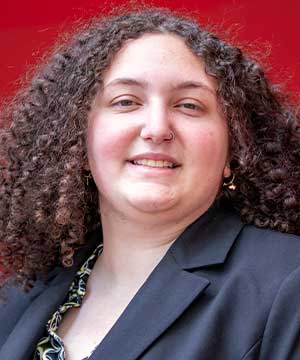 Headshot of Frankie Stella, white woman with curly brown hair. Stella smiles at the camera.