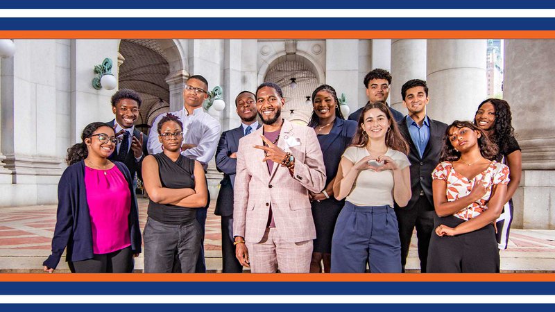 The Public Advocate poses with interns outside of the David N. Dinkins Municipal Building. The Public Advocate holds a peace sign and some interns pose with attitude, and one holds a heart shape with her hands.