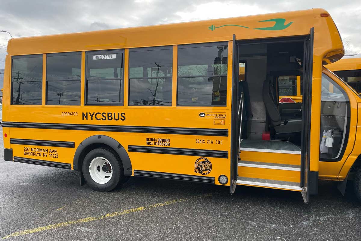 A side view of an electric yellow NYC School Bus with its doors open. 