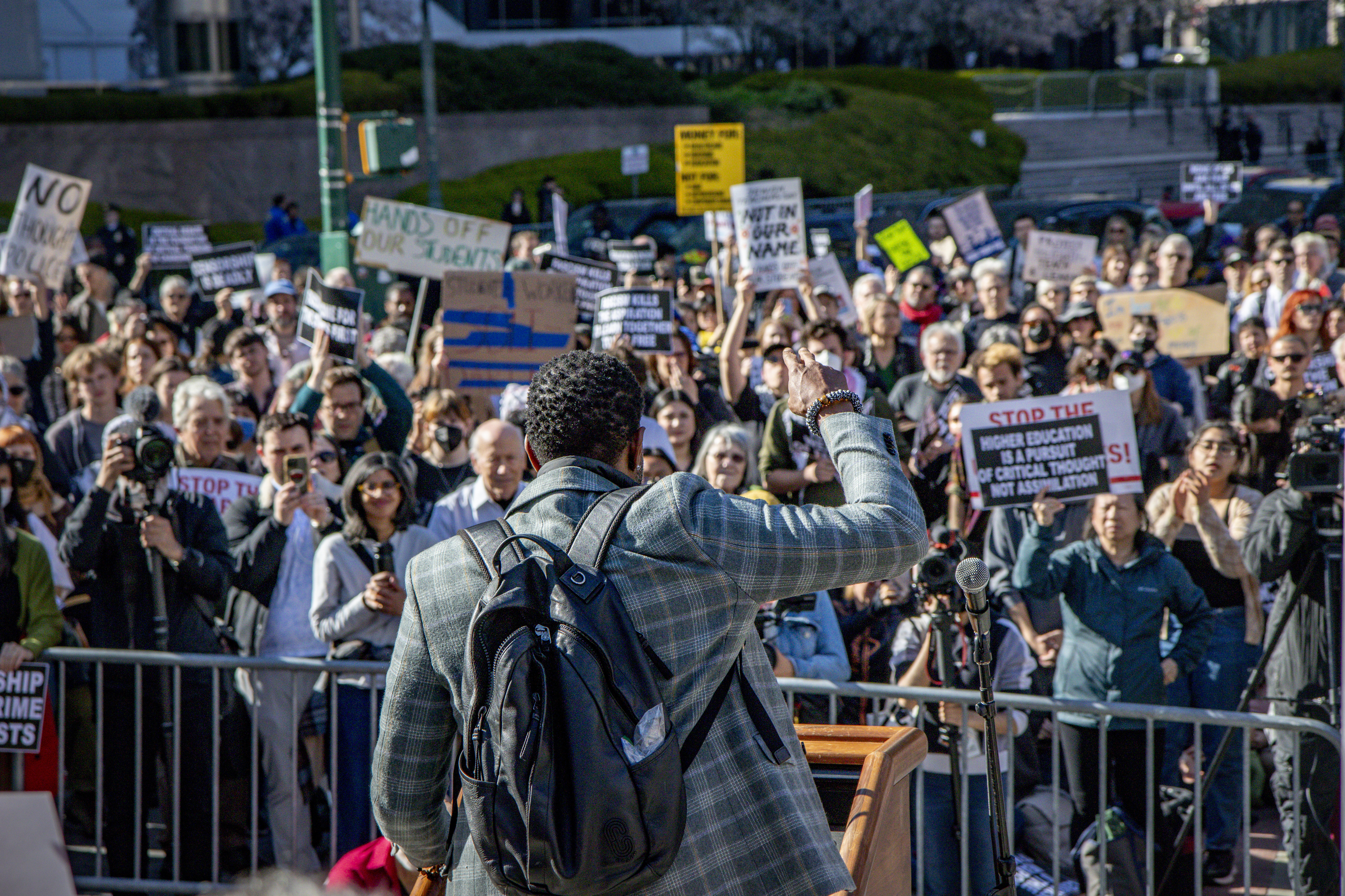 Photo of Public Advocate Jumaane D. Williams with a raise right wrist. He has his back towards us and facing a crowd of protesters.