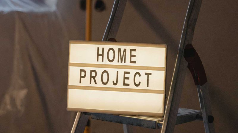 Photo of a sign with the words "Home Project" placed over a metal ladder.