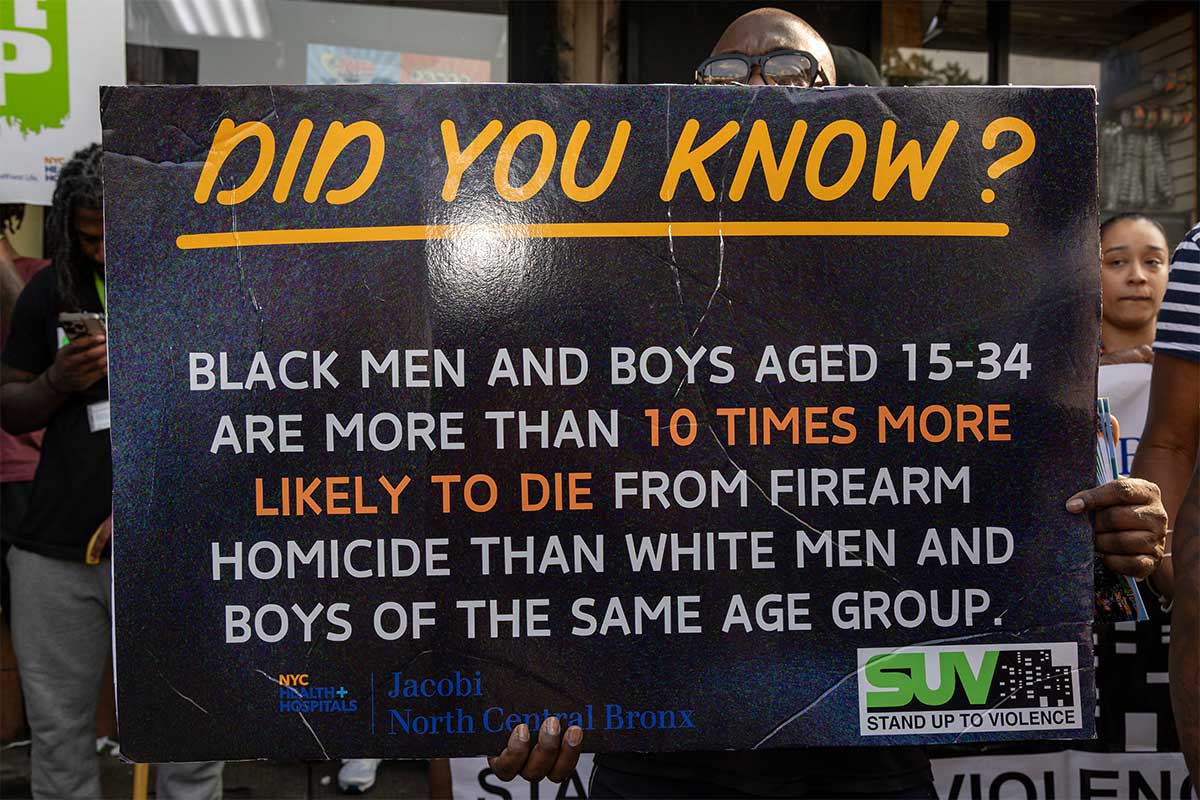 A black man holds a sign saying: "Did you know? Black men and boys aged 15-34 are more than 10 times more likely to die from firearm homicide than white men and boys of the same age group."