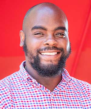 Headshot of Winston Brown, Jr. A Black man with a full beard, bald head. In a plaid red and blue shirt.