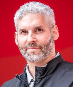 Headshot of Adam Ullian, a white male with short gray hair and a beard. Ullian glances at the camera.