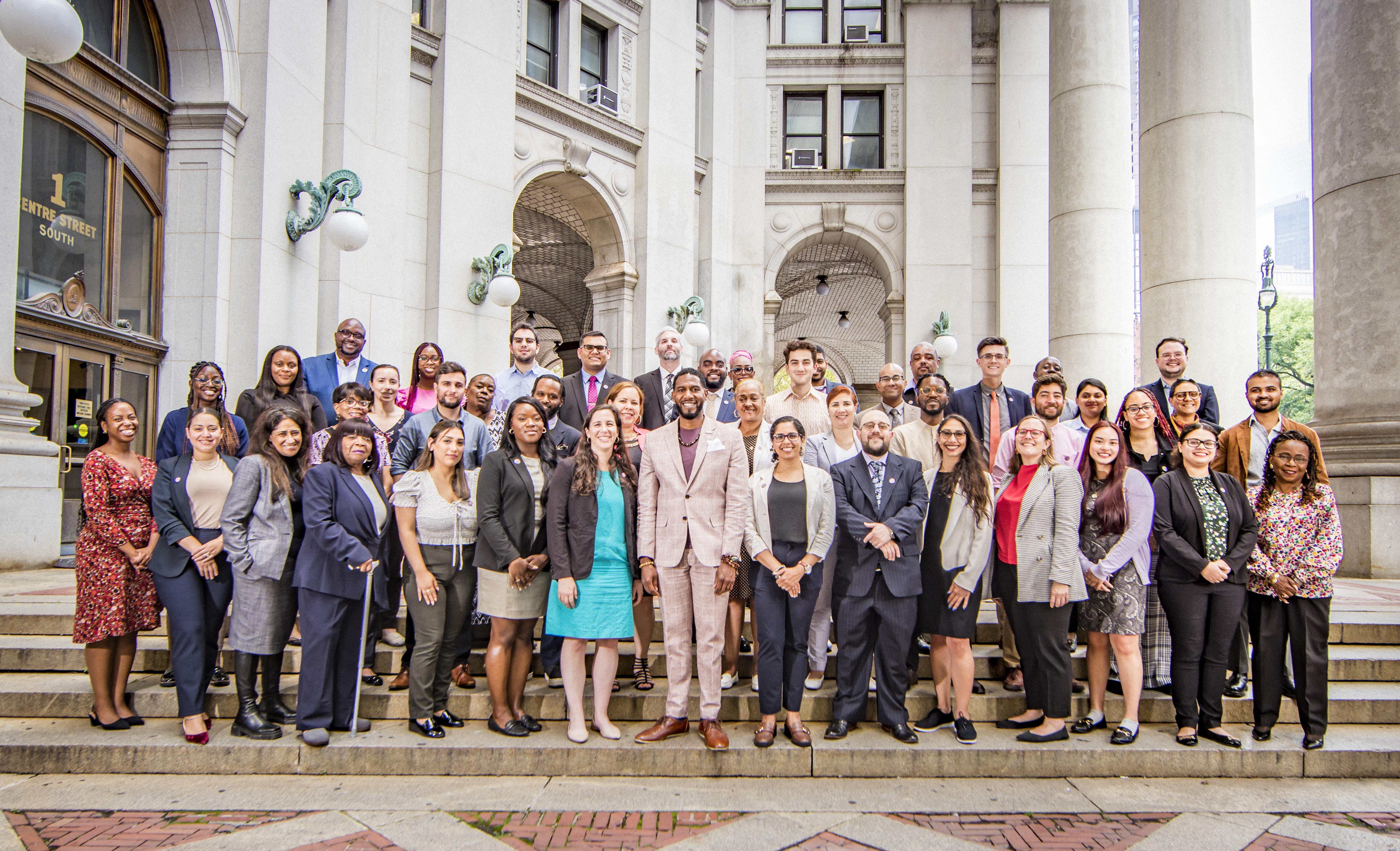 Office of the Public Advocate staff photo on the steps of 1 Centre St. Plaza, outside of the Dinkins building. The Public Advocate stands in the center of the front row, with 4 rows of staff members around him.
