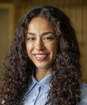 Headshot of Lindsey Bach, a woman with dark curly hair. Lindsey smiles directly at the camera.
