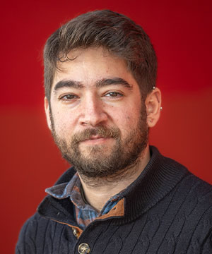 Headshot of David Kahn, a white male with short brown hair, a beard,  black-framed glasses, and a red button-down shirt. David smiles directly at  the camera.