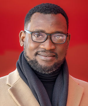 Headshot of Evans Elayelagha, a black man with short black hair and a beard wearing a black glass, smiling directly at the camera