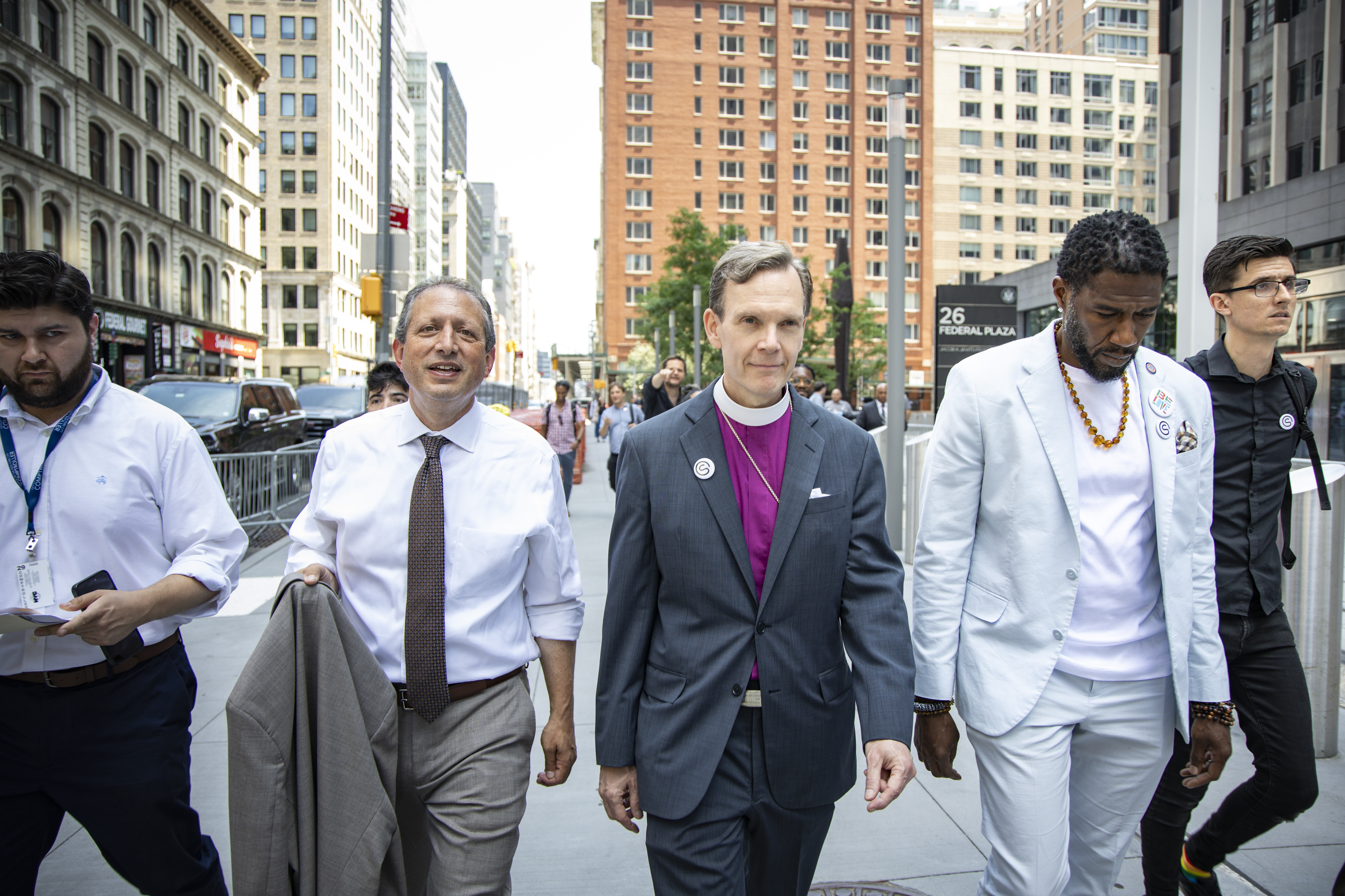 The Public Advocate, Comptroller Lander, staff member, and Bishop Heyd walk with resolution outside of 26 Federal Plaza