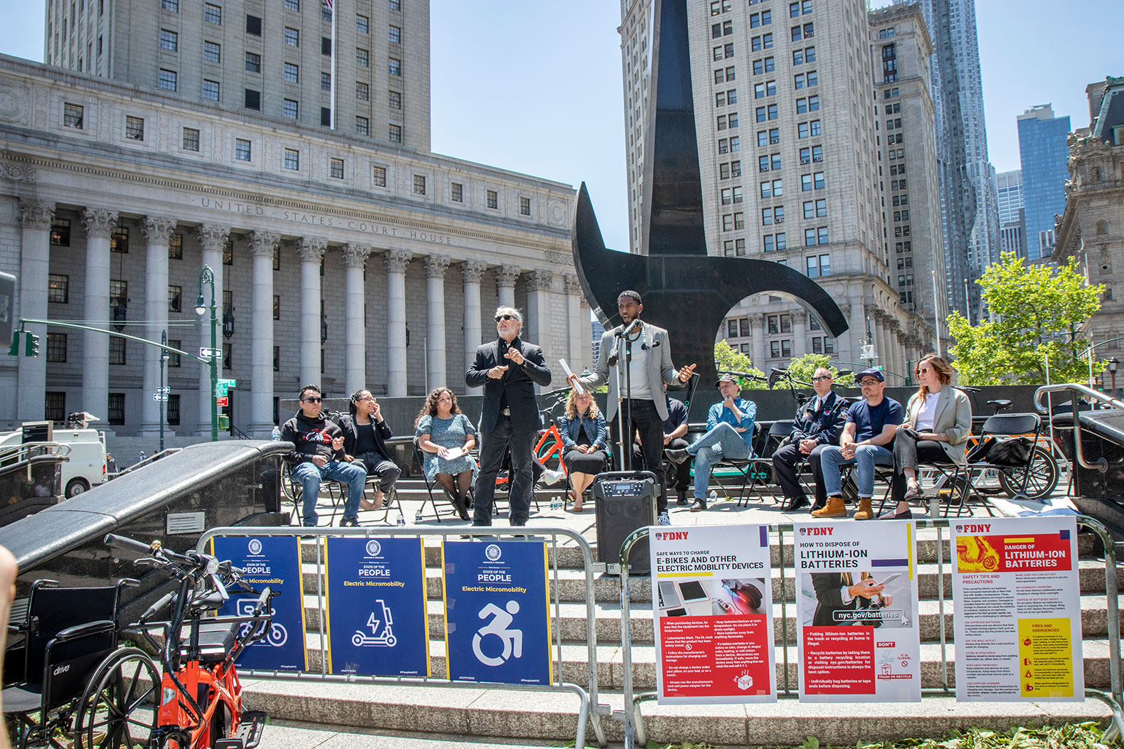The Public Advocate speaks at Foley Square as Micro Mobility advocates listen behind him. Signs for safety measures and different devices are placed at the front.