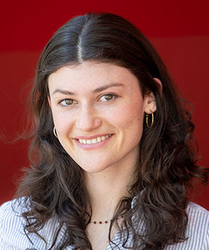 Headshot of Avery Reed, a white woman with long wavy brown hair. Avery  is wearing a striped white button down and is smiling directly at the camera.