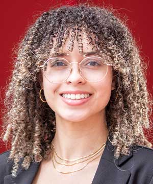 "Headshot of Marilisse Marin Longo, a white women with curly hair and glasses. Marilisse smiles brightly to the camera. "