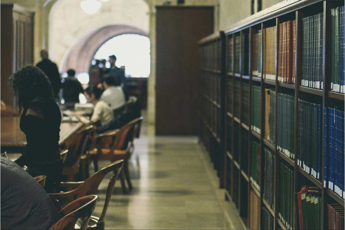 Several people at desks on the left side and a wall full of books on the right side.