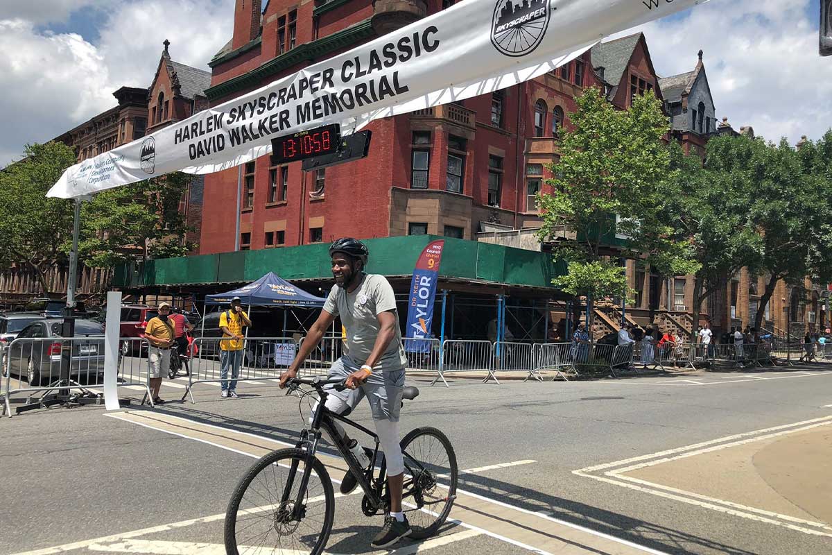 The Public Advocate, wearing a helmet, bikes across the finish line of the Harlem Skyscraper Classic David Walker Memorial.